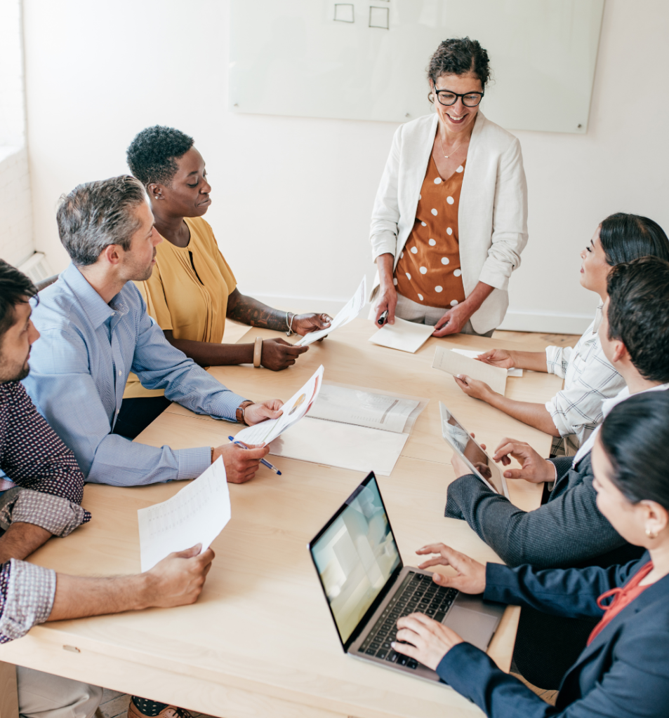 Fractional COO leading a team discussion around the conference table with documents, laptops, and shared planning materials.