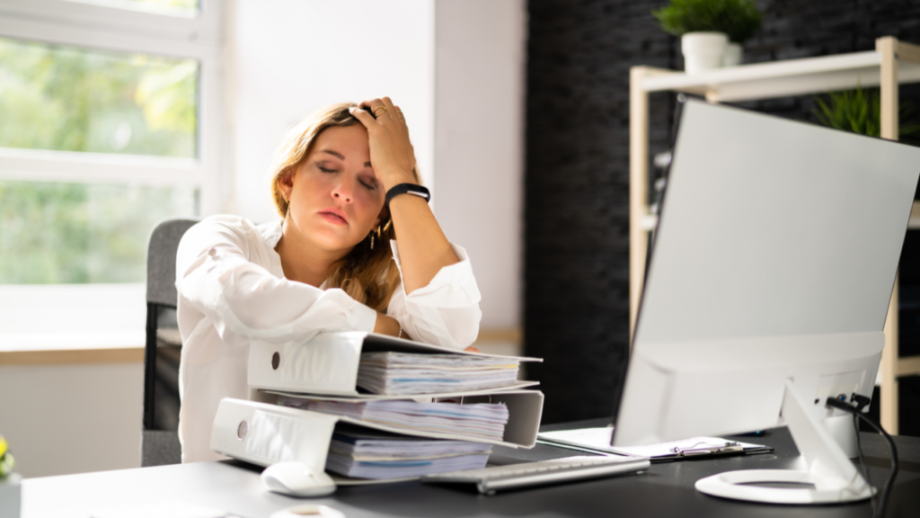 Overworked woman at office desk with binders and computer, showing decision fatigue in business.