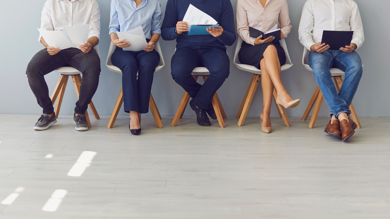 Candidates seated in a waiting area holding resumes and folders, representing the pressure of hiring faster during business growth.