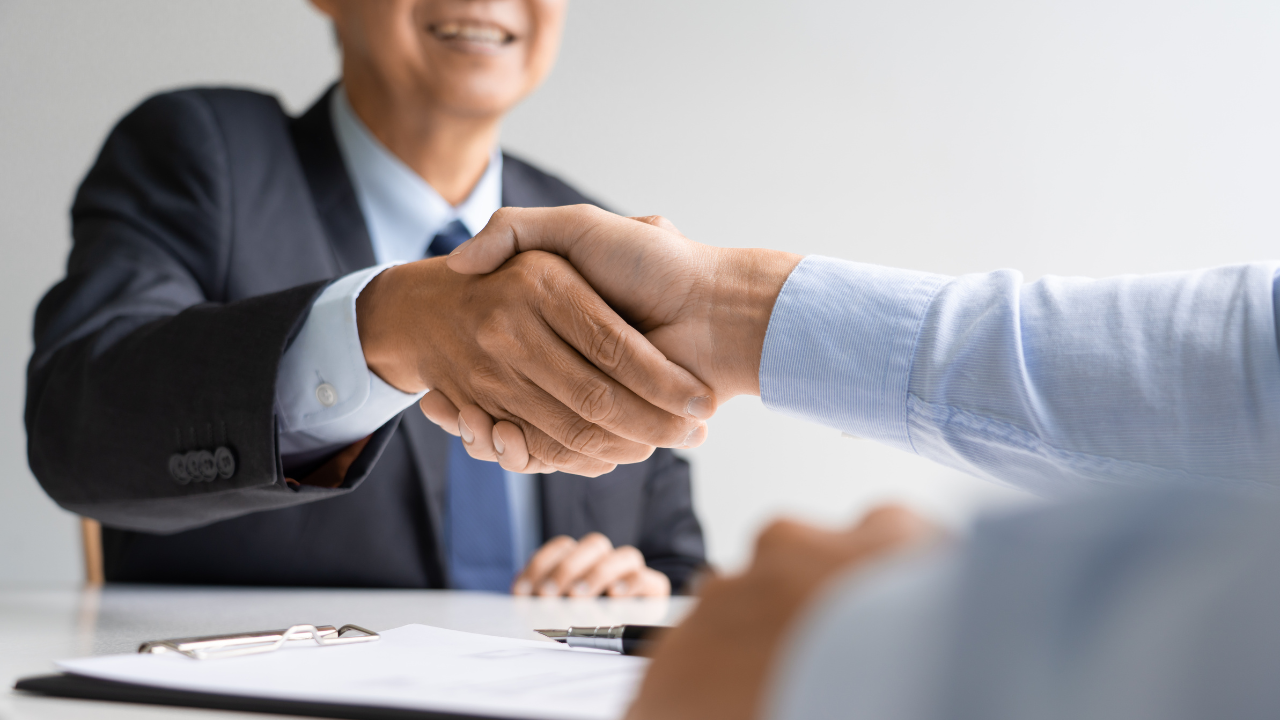 Business professionals shaking hands during a meeting, representing when to hire employees for growing company needs.