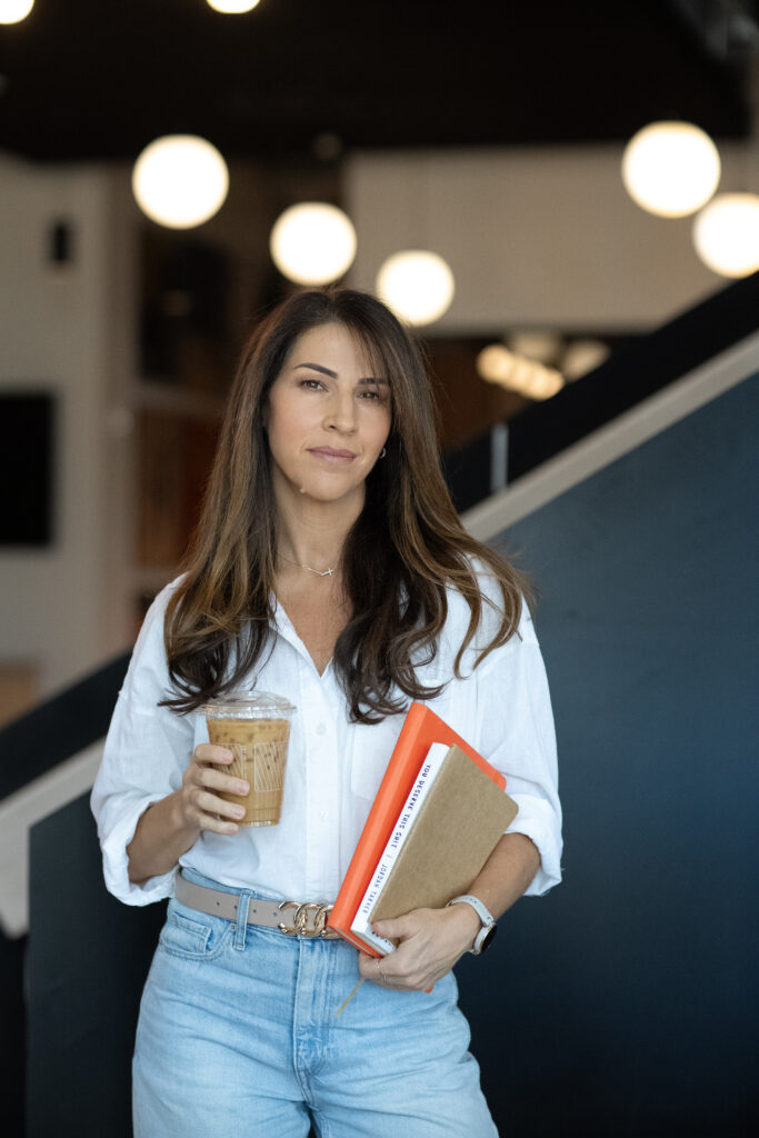 Nicole Burbank holding coffee and notebooks in a modern workspace, representing the execution gap between planning and follow-through.
