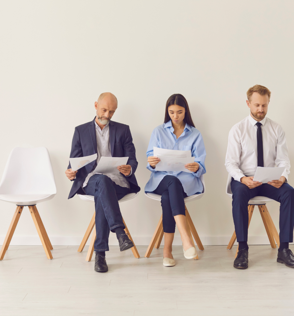 Three job candidates reviewing documents in a waiting area, representing the cost of hiring employees.