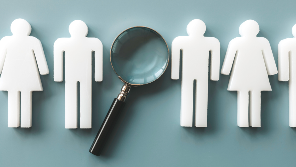 Magnifying glass examining paper employee figures, illustrating the risks of hiring too soon without clear systems.