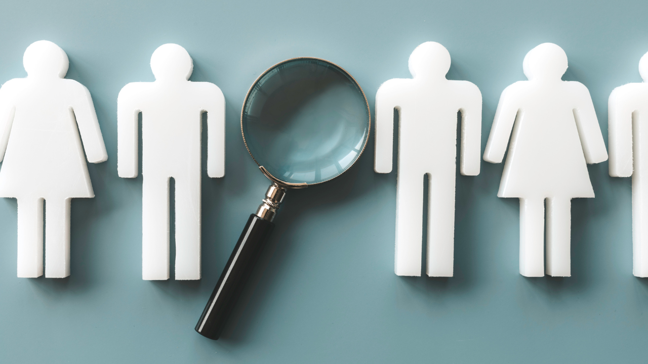 Magnifying glass examining paper employee figures, illustrating the risks of hiring too soon without clear systems.