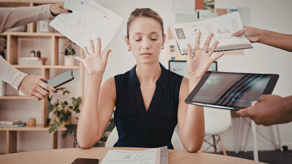 Founder overwhelm shown as a business owner sitting at her desk with eyes closed while multiple hands surround her with reports, a phone, and a tablet.