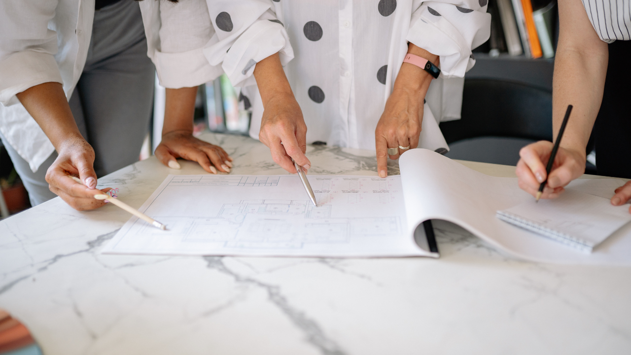 Team members review blueprints and take notes around a table during an operational planning session focused on coordinating tasks and improving business processes.