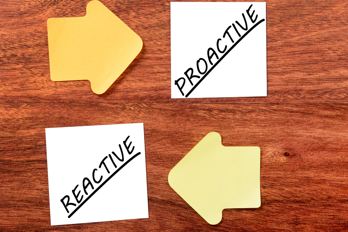 Yellow arrows point between “proactive” and “reactive” notes on a wooden surface, illustrating the shift between proactive planning and reactive operations.