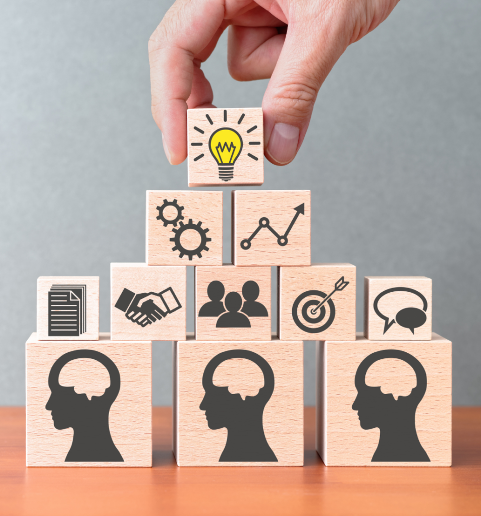 A hand stacking wooden blocks with icons representing ideas, teamwork, communication, and business growth, illustrating organizational knowledge sharing.