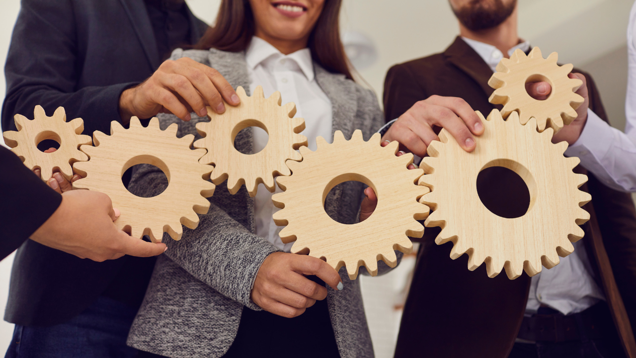 Business professionals holding interlocking wooden gears to illustrate systems vs SOPs in business operations.