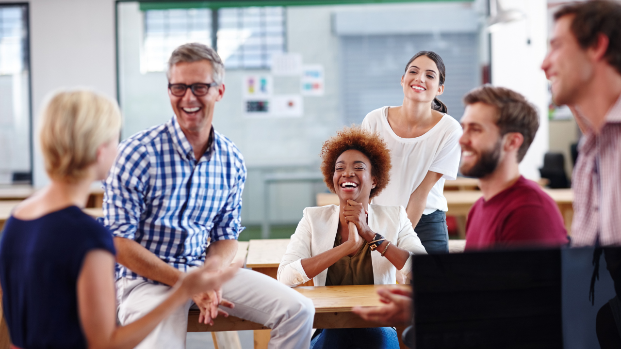 A diverse group of coworkers laughing and sharing experiences during a team discussion, highlighting tribal knowledge in the workplace and informal knowledge sharing.